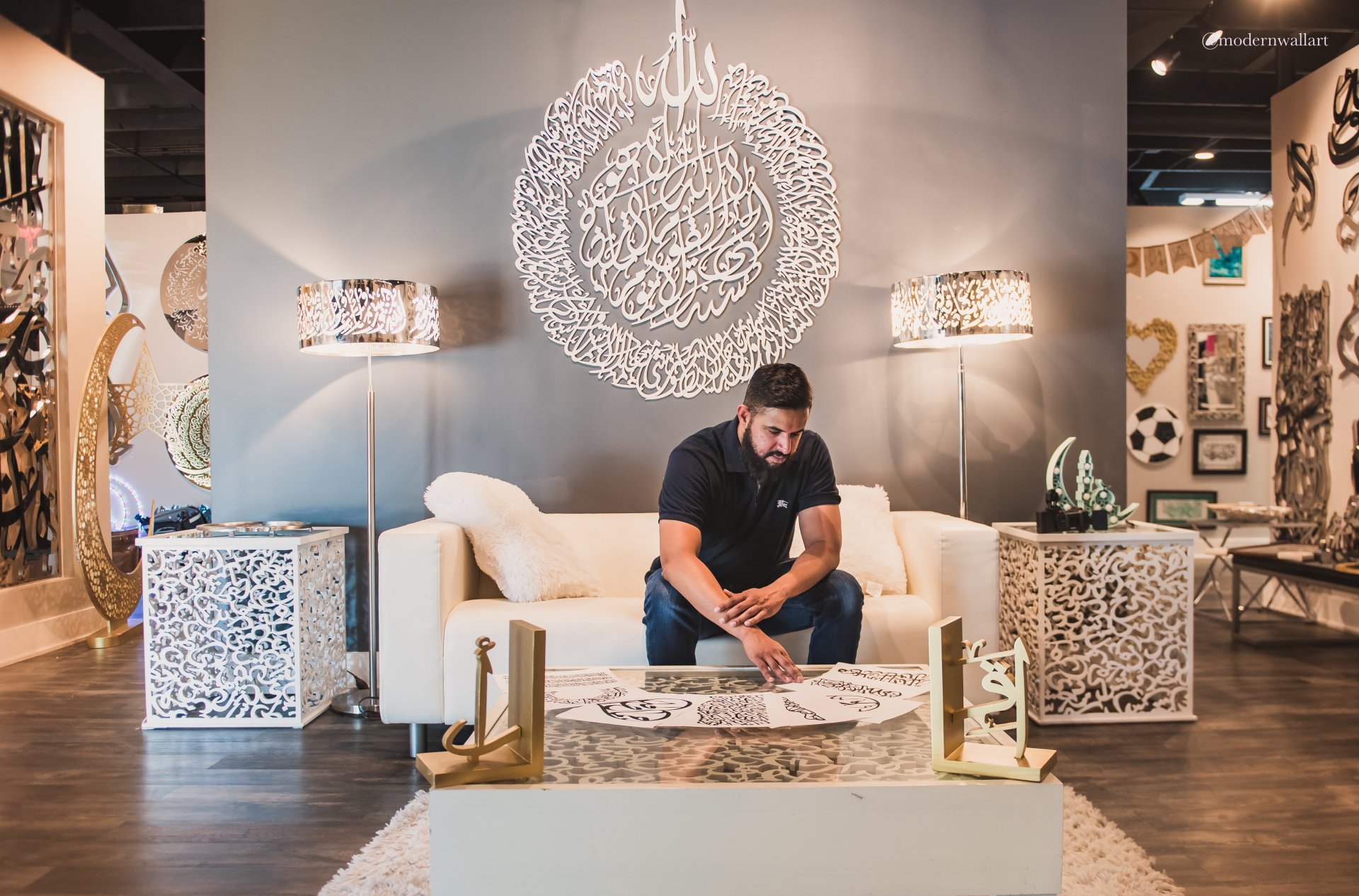 A man examines calligraphy art pieces on a glass table in a stylish gallery setting.